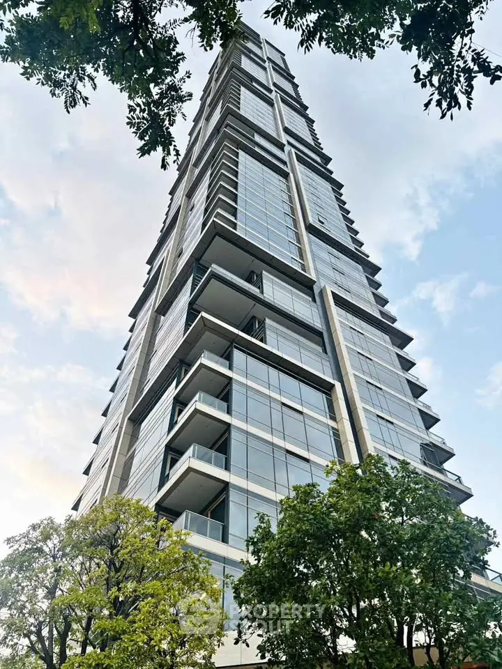 Stunning modern high-rise building with glass facade and lush greenery, perfect for urban living.
