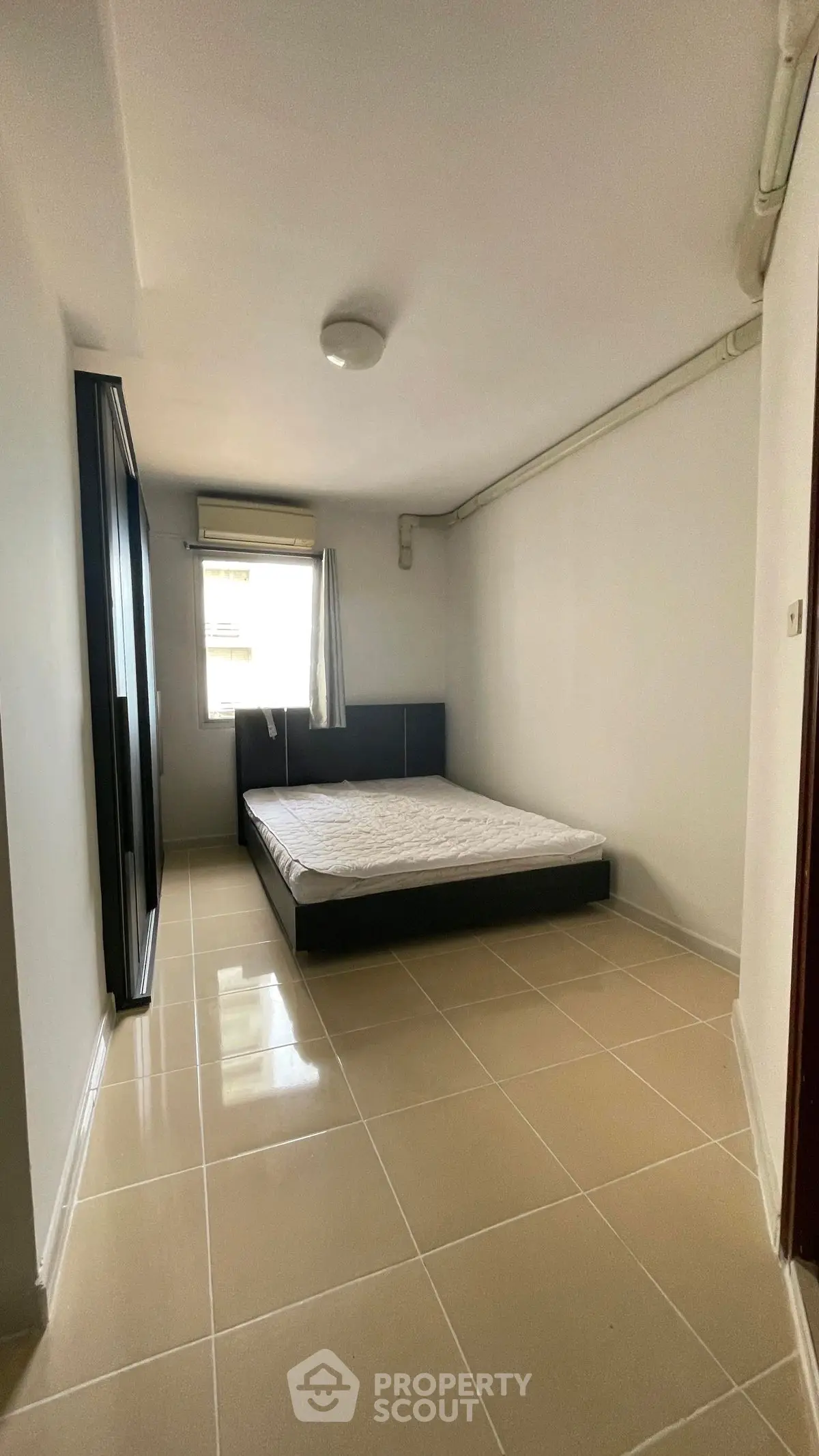 Spacious minimalist bedroom with tiled flooring and large window for natural light.