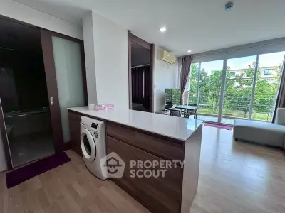 Modern open-plan living room with washing machine and large windows overlooking greenery.