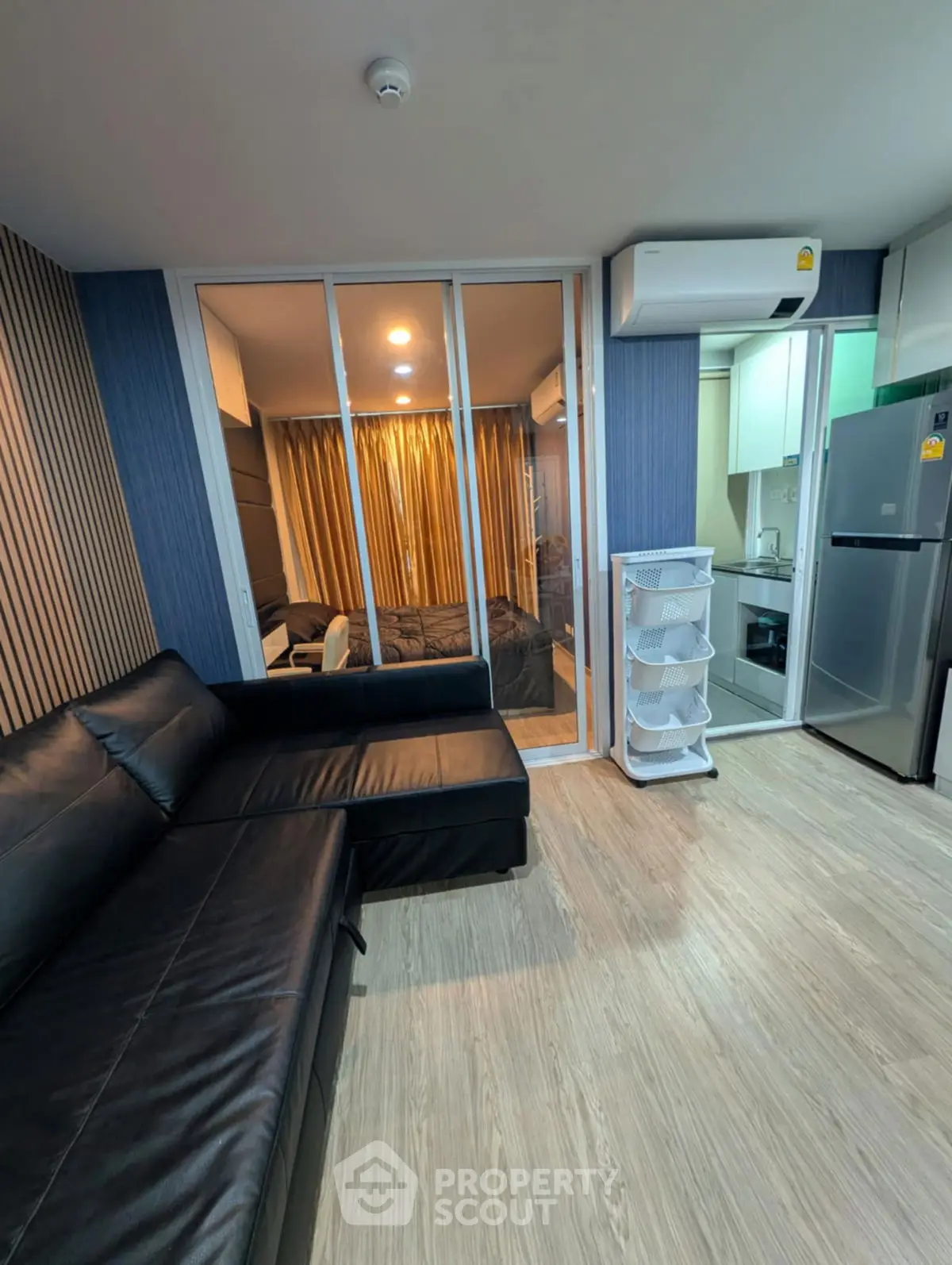 Modern living room with sleek black leather sofa and view into cozy bedroom