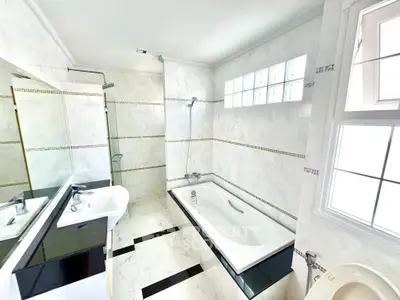 Luxurious bathroom with elegant marble tiles and modern fixtures, featuring a spacious bathtub and large window.