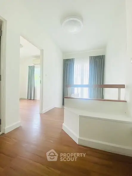 Bright and airy hallway with wooden flooring and natural light, leading to a spacious room.