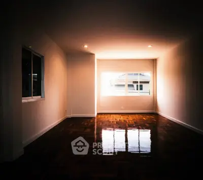 Spacious empty living room with polished wooden floors and large windows.