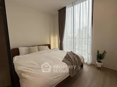 Cozy bedroom with large window and city view, featuring modern decor and natural light.