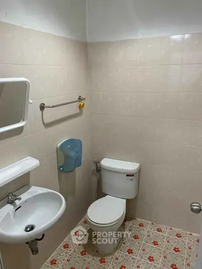 Compact bathroom with tiled walls and floor, featuring a toilet, sink, and mirror.