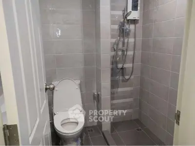 Compact modern bathroom with shower and toilet in sleek gray tiles.
