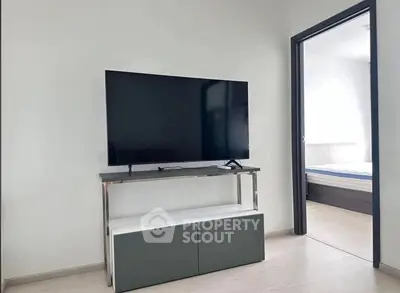 Modern living room with sleek TV stand and large flat-screen TV, leading to a bright bedroom.