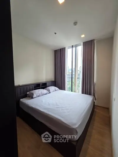 Modern bedroom with large window and city view, featuring a cozy bed and elegant curtains.