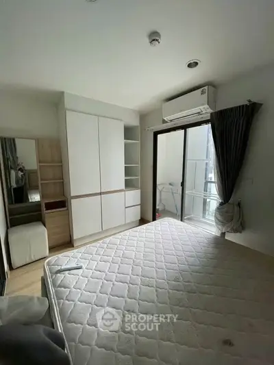 Modern bedroom with balcony access and built-in wardrobe, featuring natural light and air conditioning.