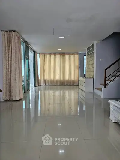 Spacious living room with large windows and modern staircase, perfect for natural light lovers.