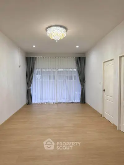 Spacious empty living room with elegant chandelier and large windows with curtains.