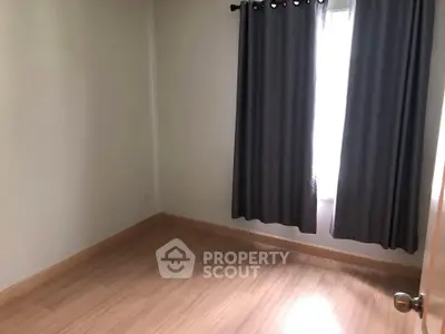 Spacious empty bedroom with wooden flooring and large window.