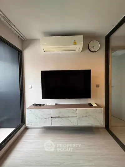 Modern living room with sleek TV setup and air conditioning, featuring minimalist design and natural light.