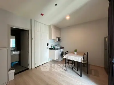 Modern apartment interior with compact kitchen and dining area, featuring washing machine and fridge.