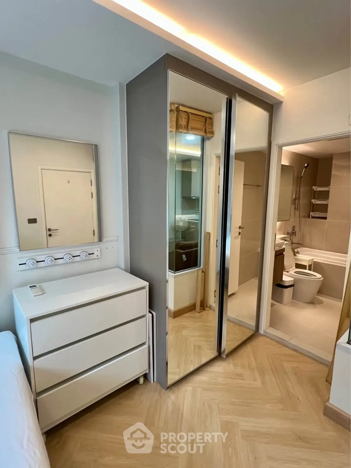 Modern bedroom with mirrored wardrobe and ensuite bathroom, featuring sleek design and ample storage.