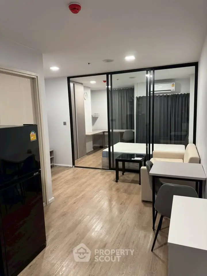 Modern apartment interior with glass partition, cozy seating, and sleek flooring.