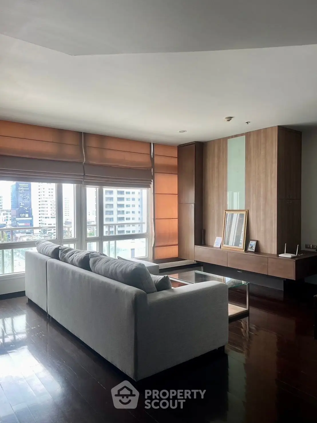 Spacious modern living room with large windows and city view, featuring a sleek sofa and wooden accents.