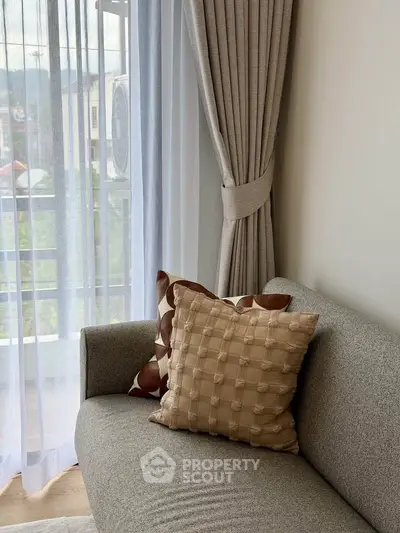 Cozy living room with elegant gray sofa and decorative pillows near a sunlit window with sheer curtains.