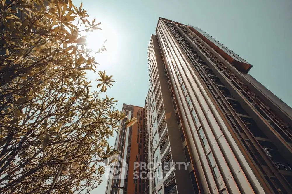 Modern high-rise building with sleek architecture and lush greenery under a clear sky.