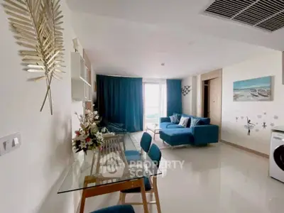 Modern living room with stylish decor and glass dining table, featuring blue sofa and natural light.