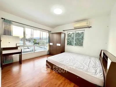 Spacious bedroom with large windows and wooden flooring, offering a bright and airy atmosphere.