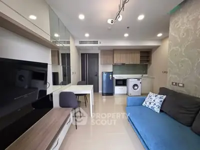 Modern living room with blue sofa, TV, and kitchen appliances in open layout.