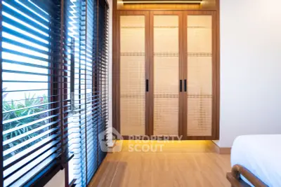 Elegant bedroom with wooden wardrobe and large windows with blinds, offering a serene and modern ambiance.