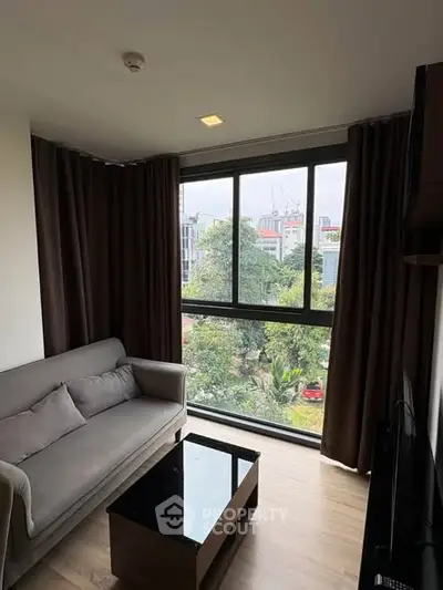 Cozy living room with large window offering a lush green view, modern sofa, and sleek coffee table.