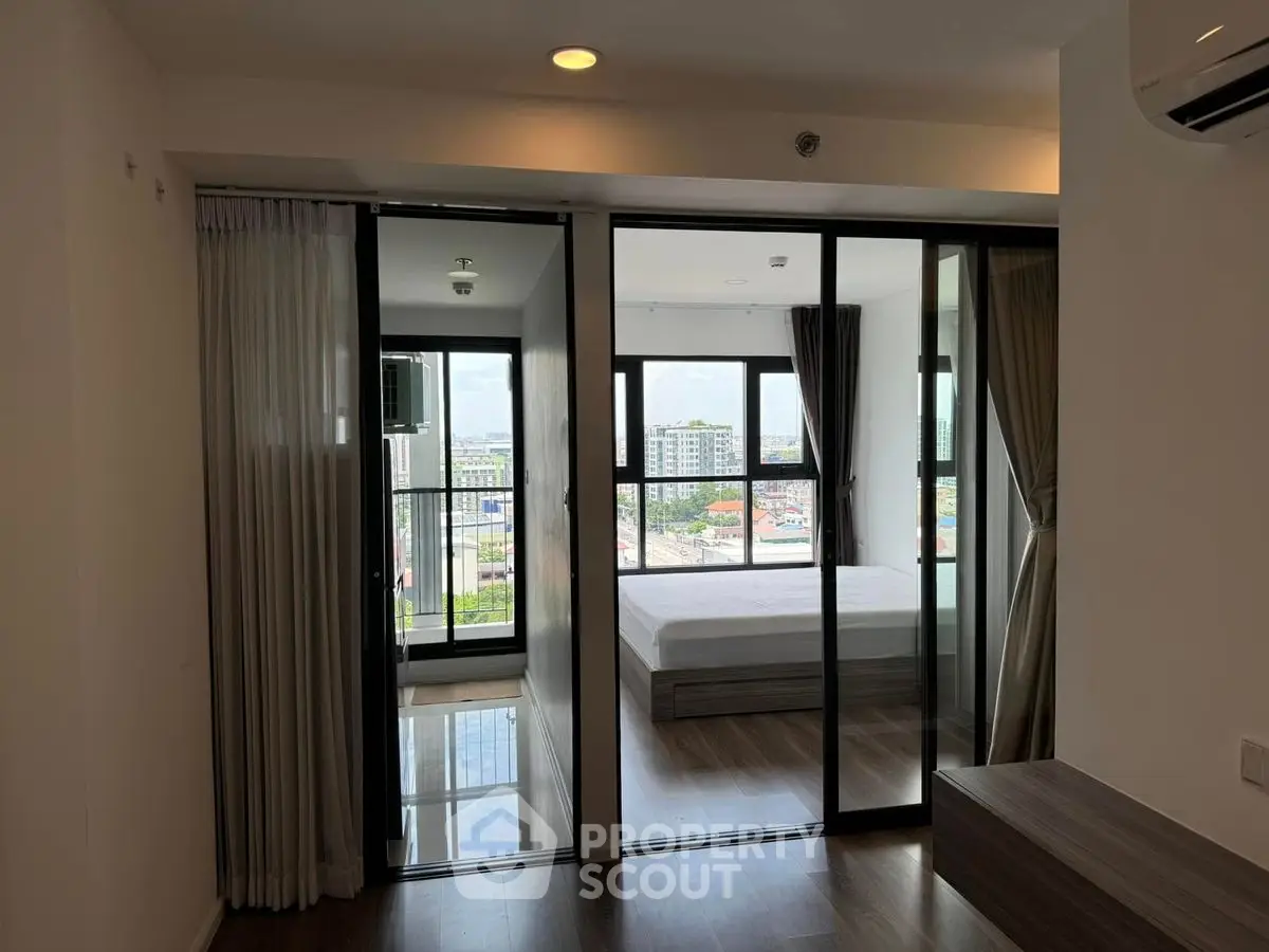 Modern apartment with glass partition and city view, featuring a cozy bedroom and sleek flooring.