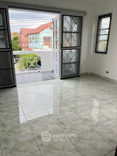 Spacious tiled room with open doors leading to a balcony, offering a bright and airy atmosphere.