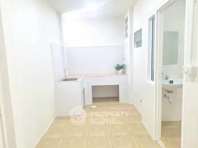 Minimalist kitchen with white walls and wooden countertops, featuring a small sink and potted plant.