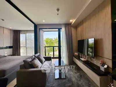 Modern living room with sleek design and large TV, featuring a view of the balcony and greenery.