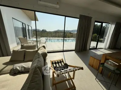 Luxurious open-plan living space with expansive glass doors leading to a serene pool, offering a seamless indoor-outdoor living experience.