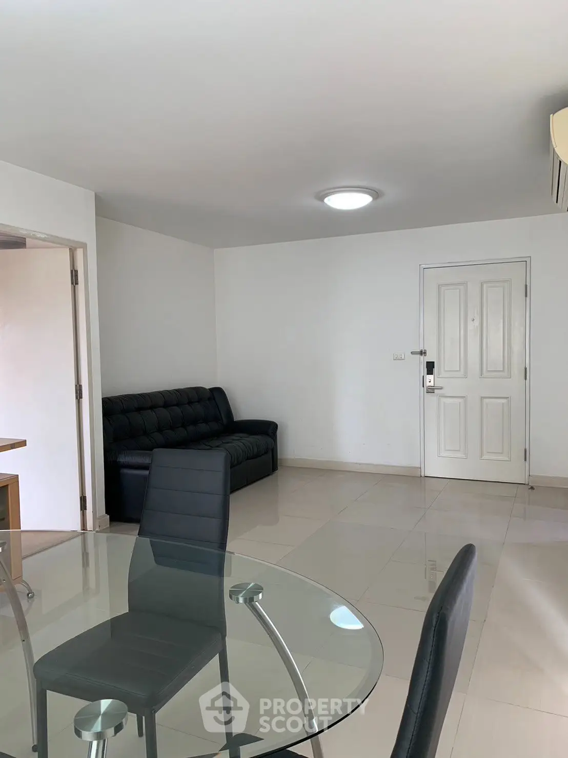 Modern living room with sleek glass dining table and black leather sofa, featuring minimalist design and bright lighting.