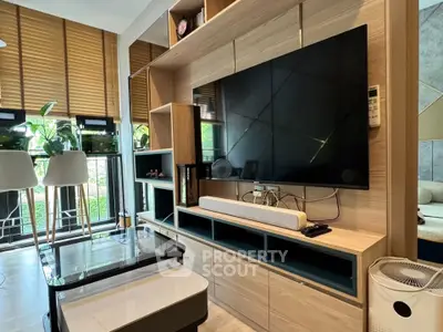 Modern living room with large TV, stylish shelving, and natural light from balcony.