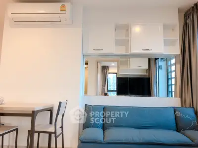 Modern living room with blue sofa, wall-mounted air conditioner, and sleek cabinetry.