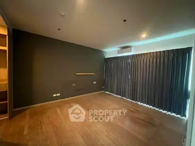 Spacious empty room with wooden flooring and large window, ideal for customization.