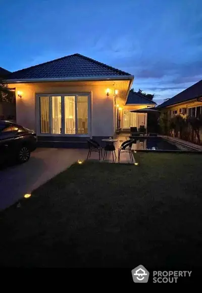 Charming evening view of a cozy house with illuminated patio and poolside seating.