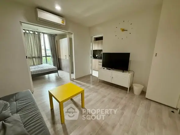 Modern living room with yellow coffee table and TV, open layout to bedroom and kitchen.