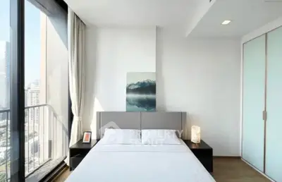 Modern bedroom with large windows and city view, featuring minimalist decor and ample natural light.