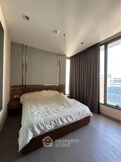 Spacious bedroom with large windows and modern decor in a high-rise building.