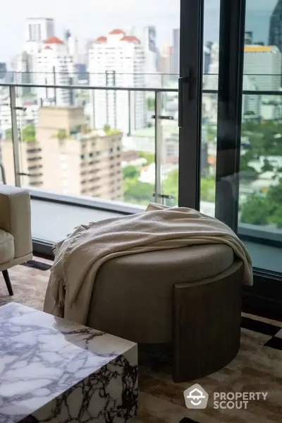 Luxurious high-rise corner unit with floor-to-ceiling windows offering panoramic city views, complemented by a plush ottoman and elegant marble table.