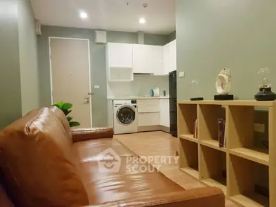 Modern living room with leather sofa and integrated kitchen featuring washing machine.