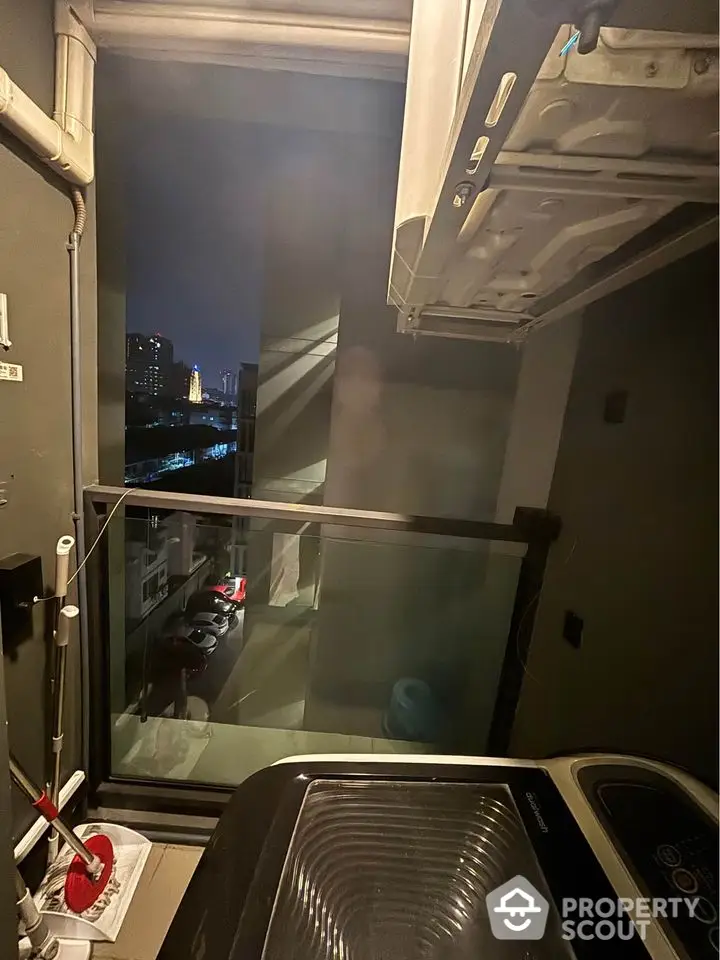 Modern apartment balcony with washing machine and city view at night.