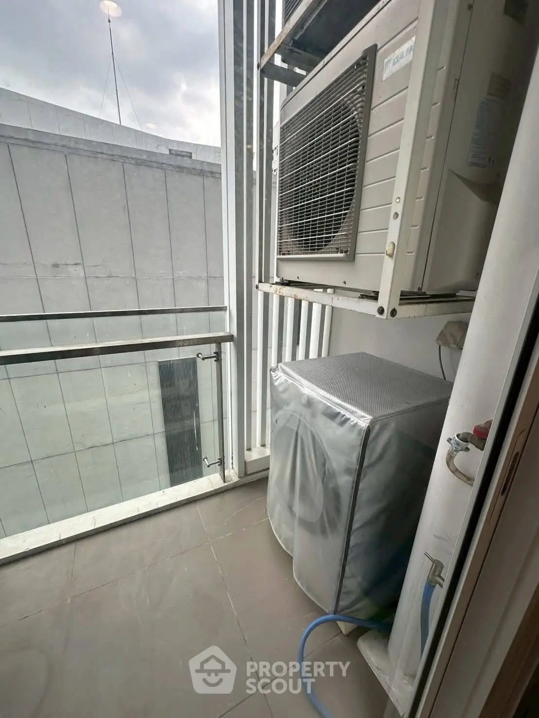 Compact balcony with washing machine and air conditioning unit in modern apartment.