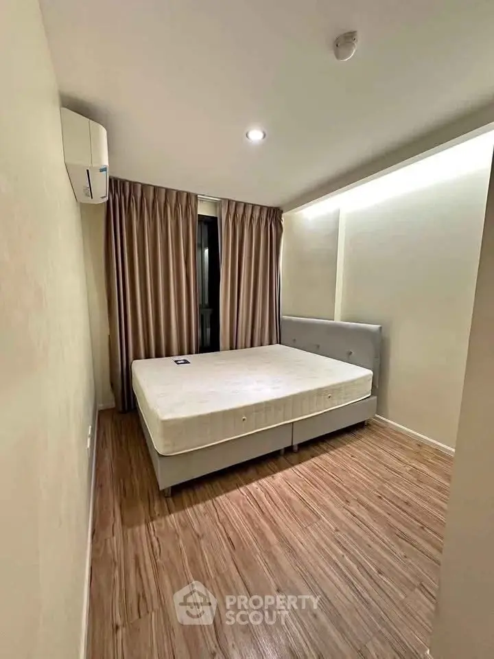 Cozy bedroom with wooden flooring and natural light, featuring a comfortable bed and elegant curtains.