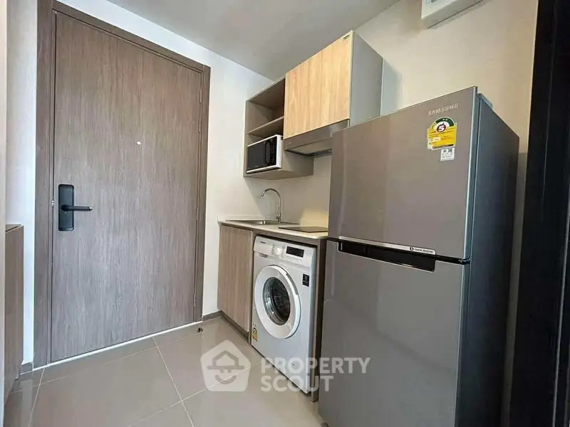 Compact modern kitchen with washing machine and fridge in stylish apartment.