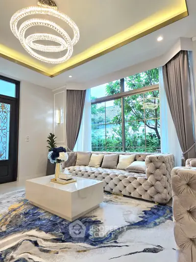Luxurious living room with elegant chandelier and plush sofa, featuring large windows and modern decor.