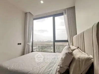 Bright bedroom with large window offering city view, modern decor and cozy ambiance.