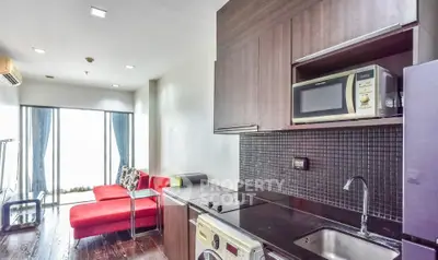 Modern apartment with sleek kitchen and cozy living area featuring red sofa and large windows.